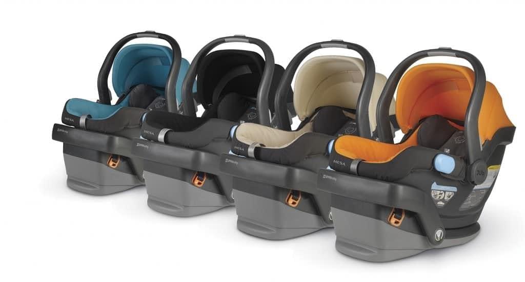 Four infant car seats in teal, black, beige, and orange colors are lined up in a row, resembling a tidy lineup of cozy taxi car seats.