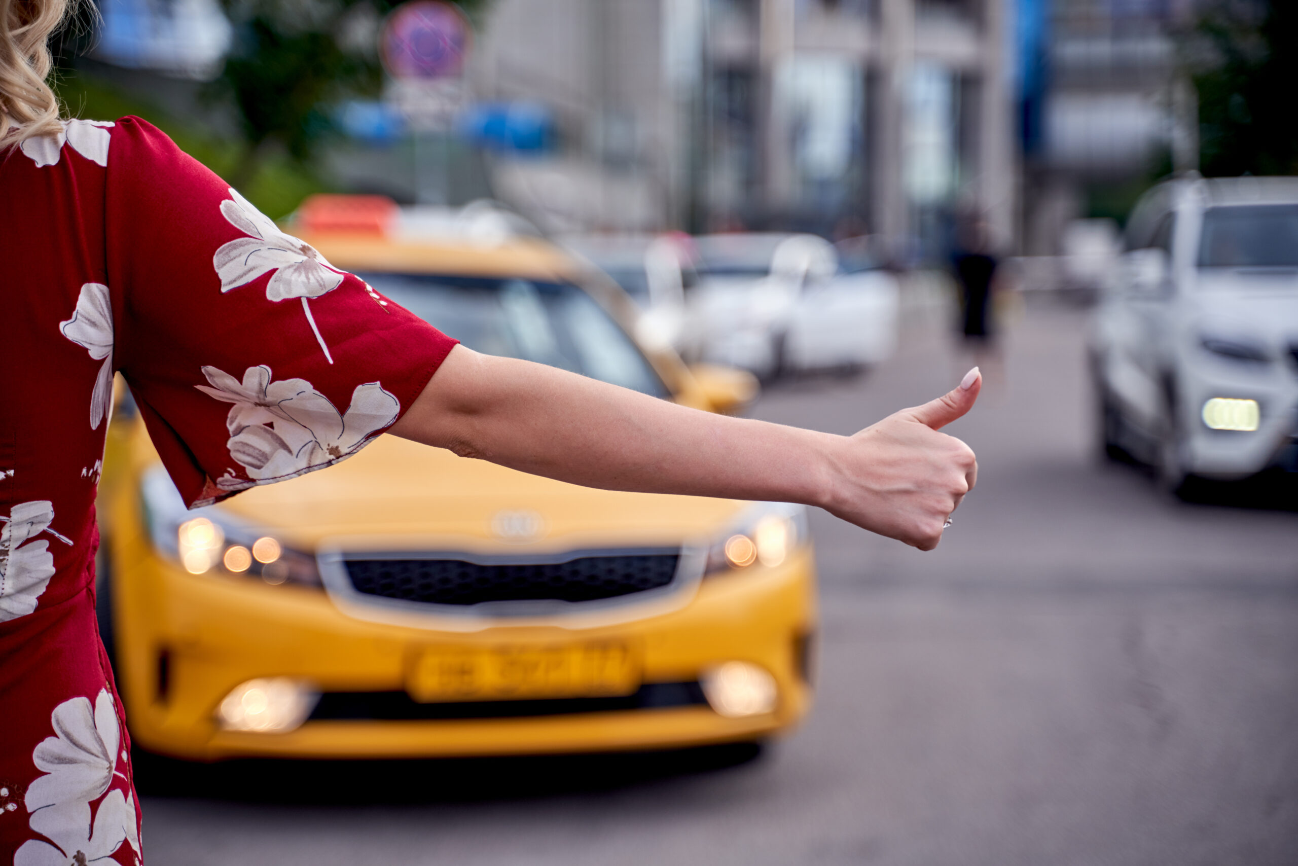 Picture from back of woman with outstretched hand stopping taxi in afternoon on blurred background of modern city