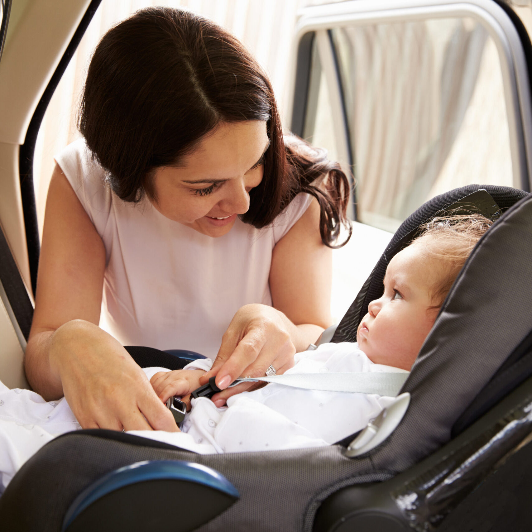 A woman fastening a baby in a car seat inside a DFW taxi, with both looking at each other.