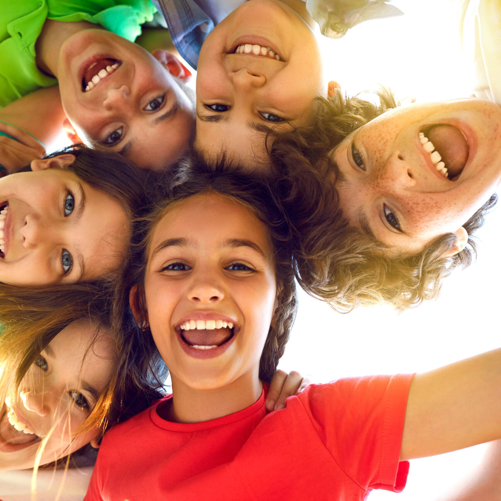 Bunch of cheerful joyful cute little children playing together and having fun. Group portrait of happy kids huddling, looking down at camera and smiling. Low angle, view from below. Friendship concept